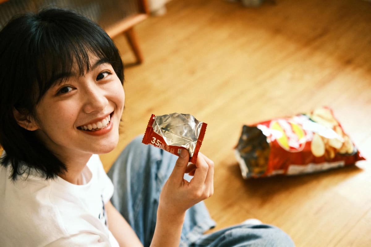 An empty 3.5g snack wrapper next to a happy consumer, with a nearly full, forgotten large bag of snacks in the background