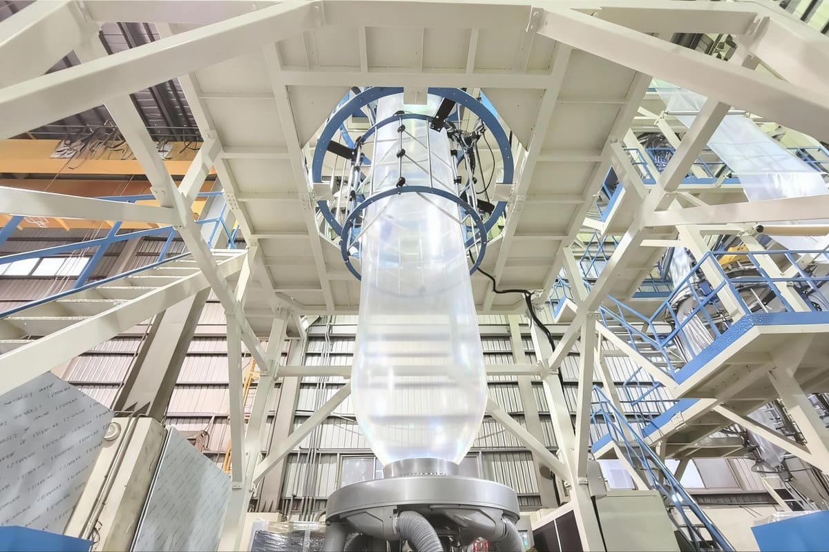 A large, transparent "bubble" of plastic film rising high above an extruder machine in a factory